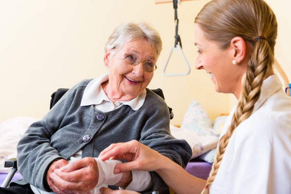 Nurse taking care of senior woman in retirement home bandaging a nursing home caretaker insurance